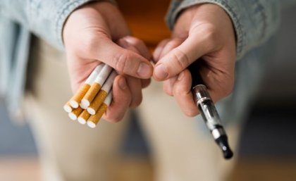 Two hands - one holding a pack of traditional cigarettes, the other holding a vape